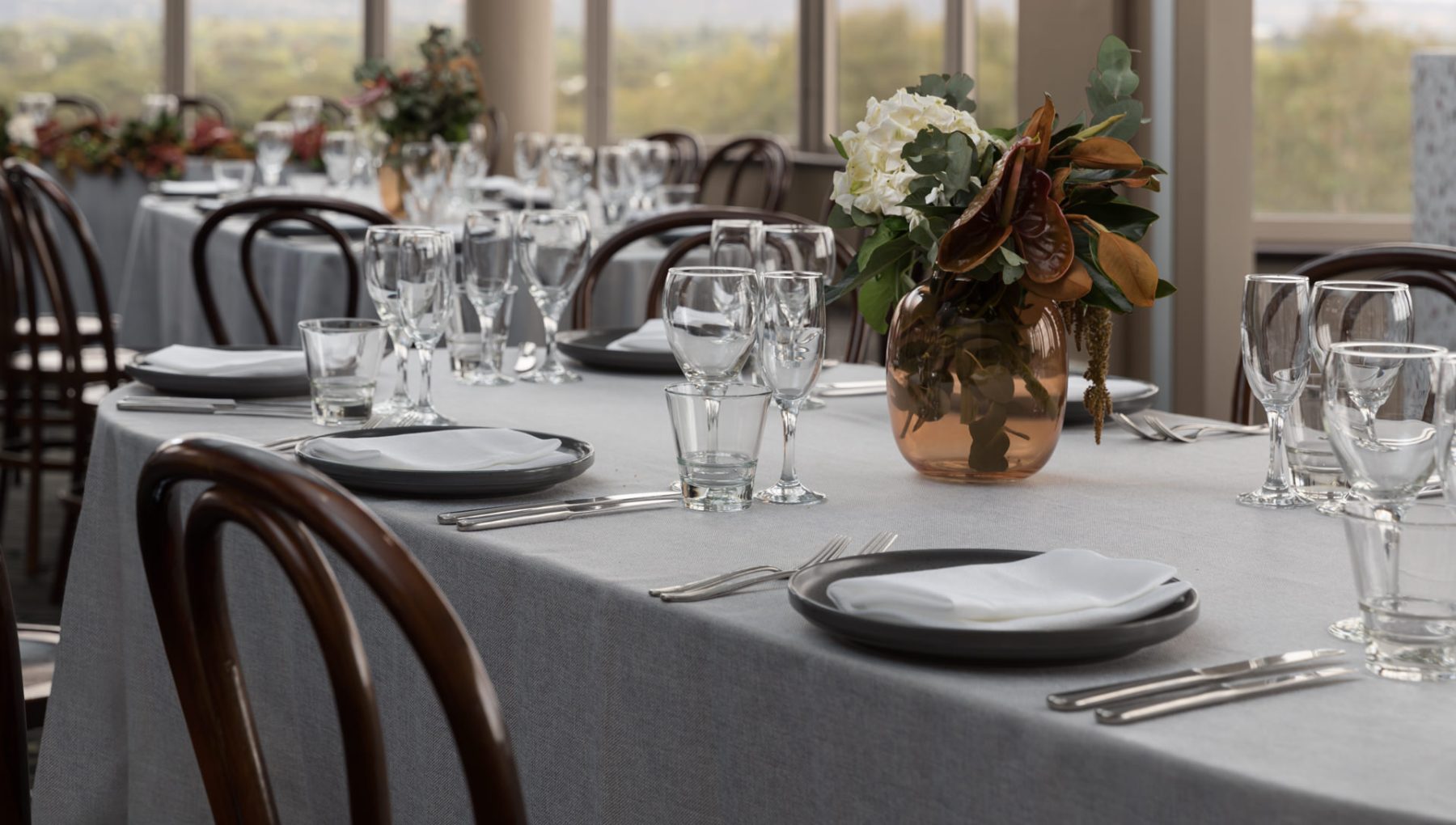 A dining table set with gray tablecloth, plates, utensils, and various glassware, featuring a floral centerpiece.