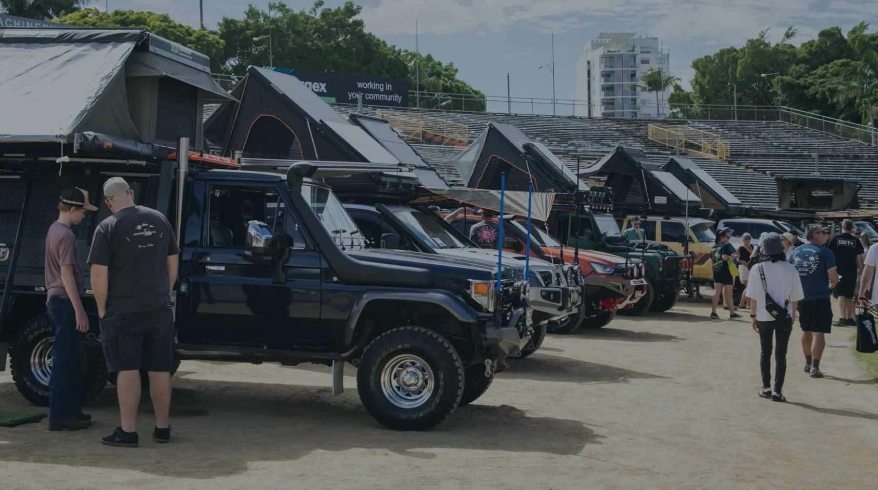 A row of off-road vehicles with rooftop tents is displayed at an outdoor event, with attendees interacting and exploring.