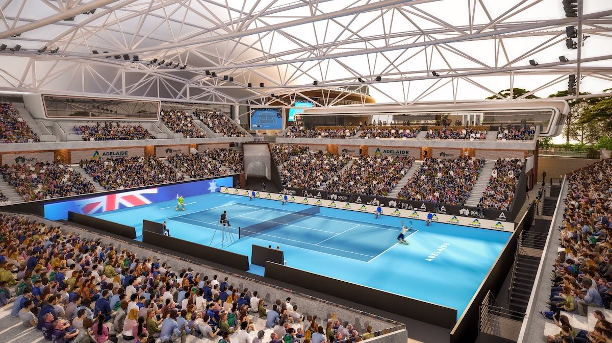 A crowded indoor tennis arena with players on a bright blue court beneath a white truss roof.