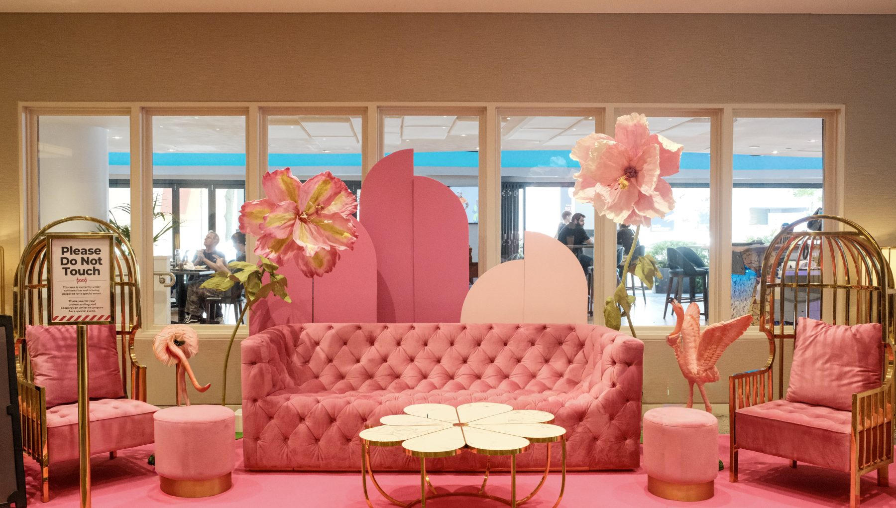 Pink velvet sofas and gold tables sit beneath oversized paper flowers in a lounge with a flamingo decoration.