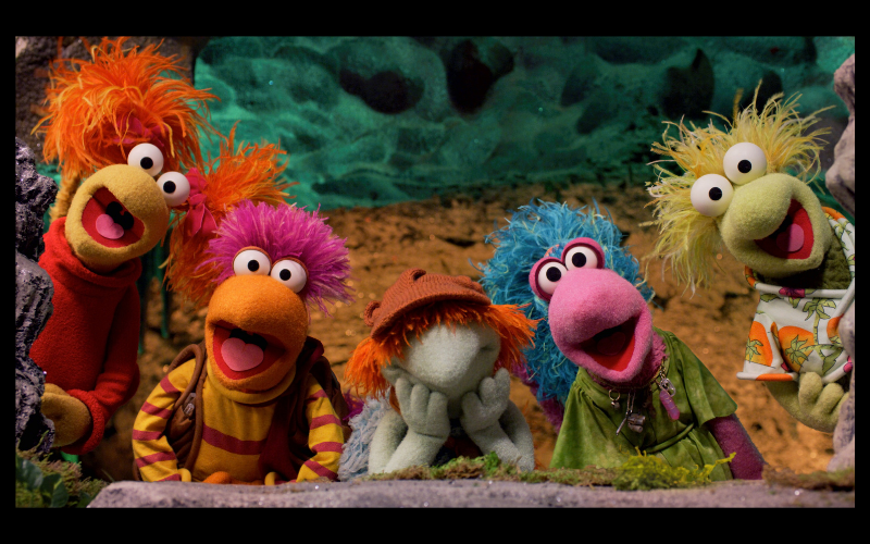 Five colorful puppets with bright hair and varied expressions gather together, posed playfully against a textured background.