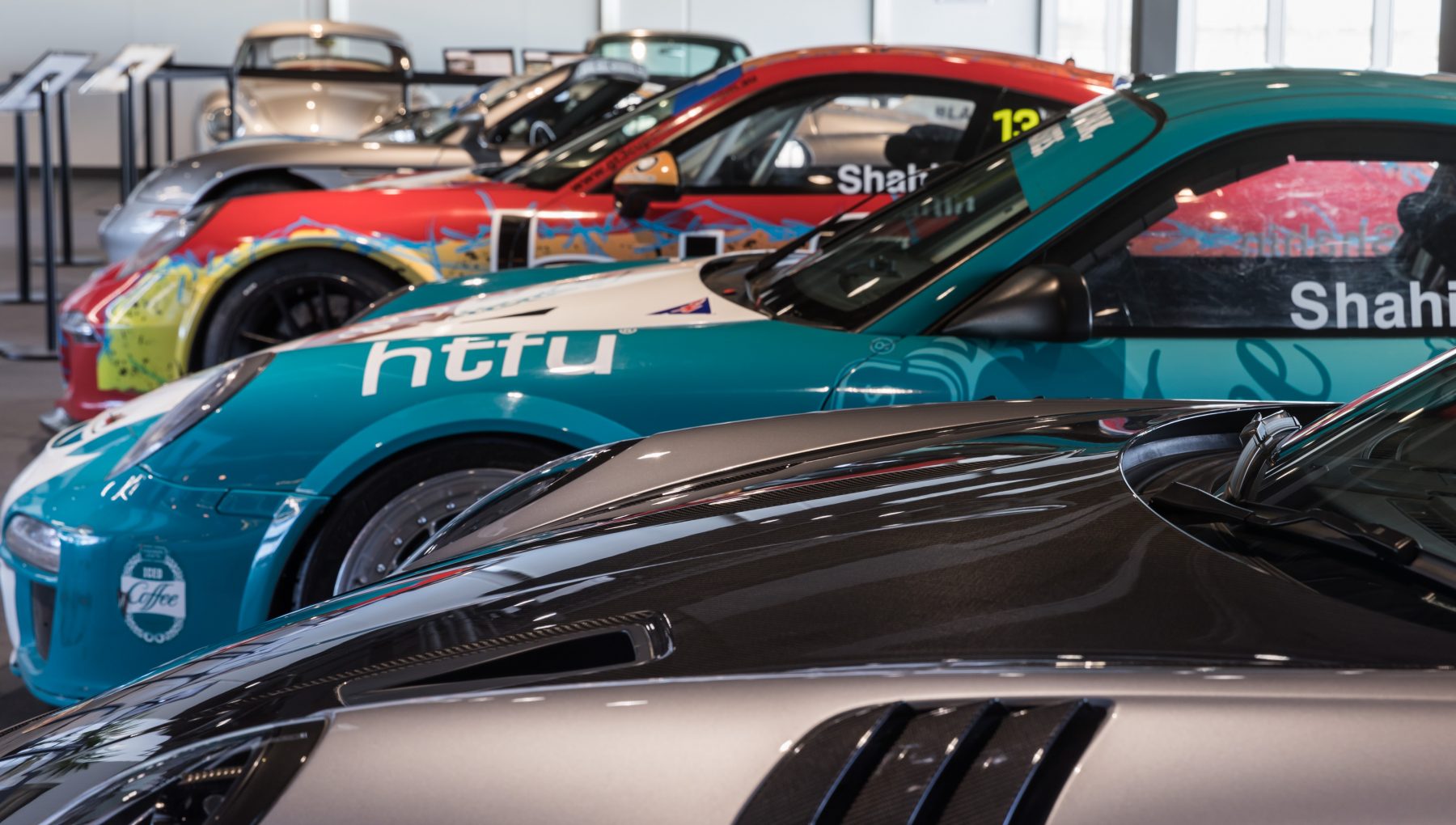 A row of colorful racing cars is displayed in a showroom, featuring various designs and angles, showcasing their sleek profiles.