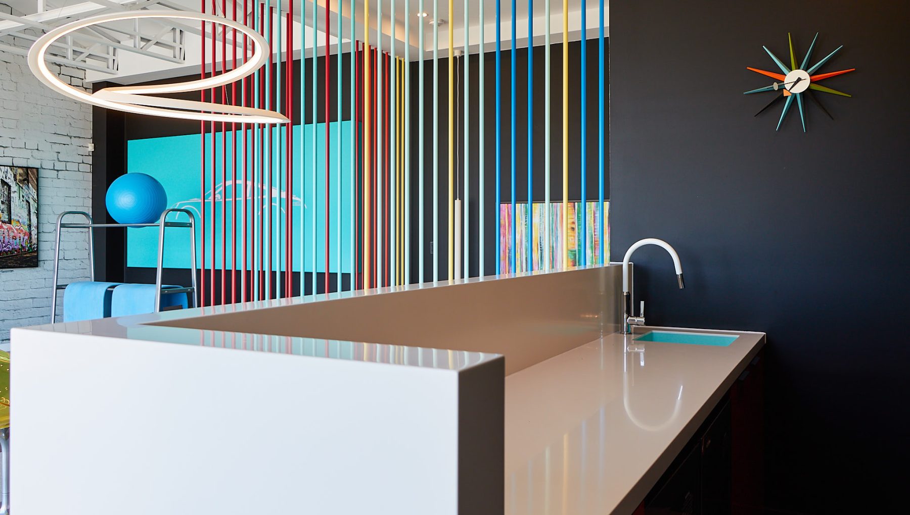 Modern kitchen space featuring a sleek white countertop, colorful vertical accents, and a clock on a black wall.