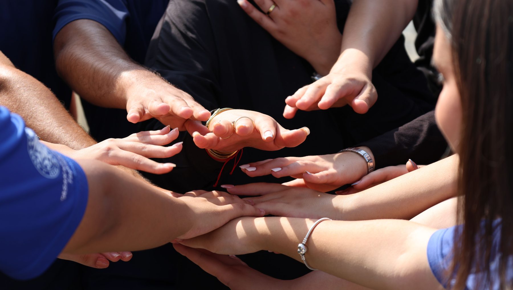 Several people extend their arms and stack their hands together in a group huddle.