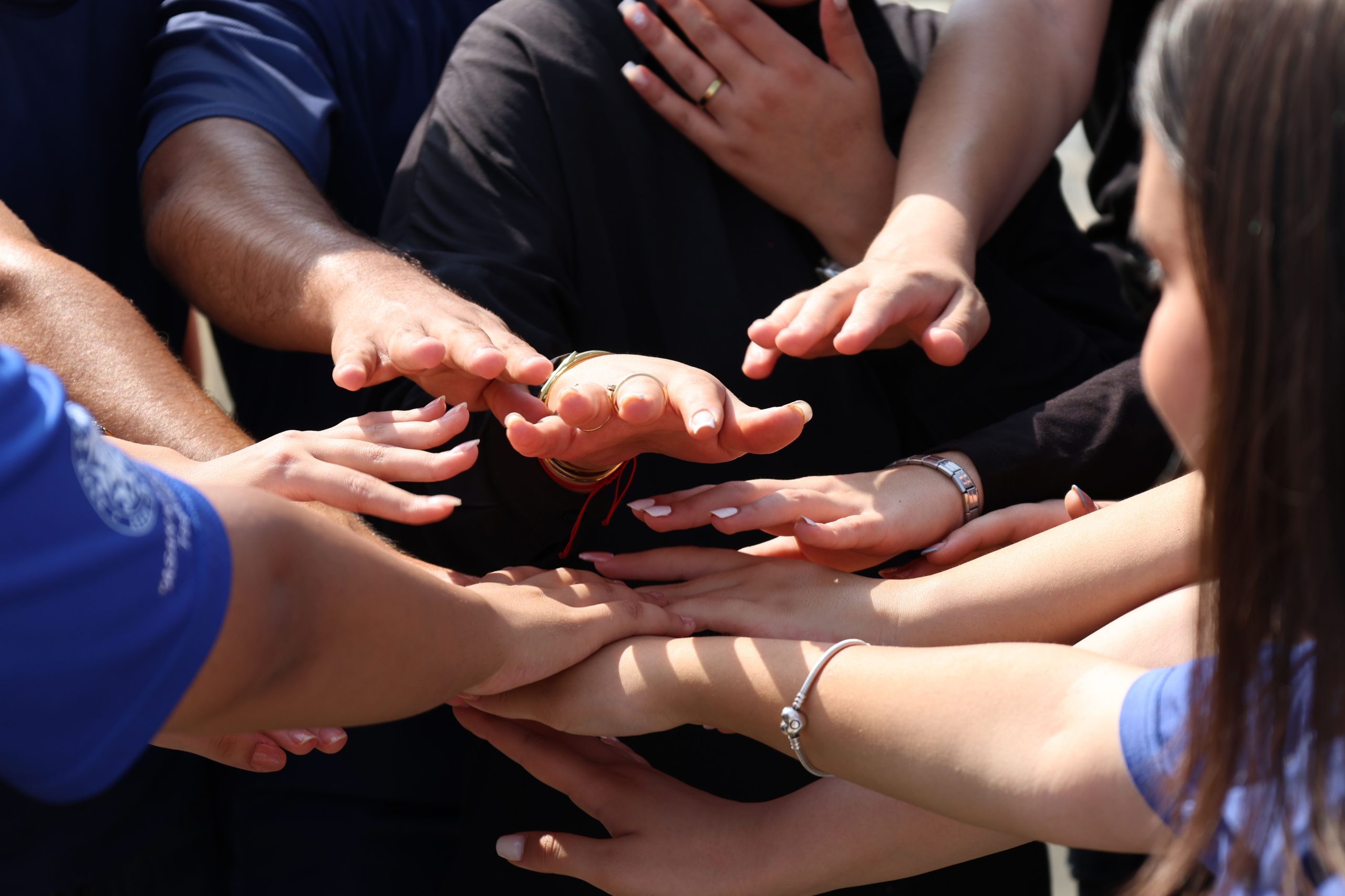 Several people extend their arms and stack their hands together in a group huddle.