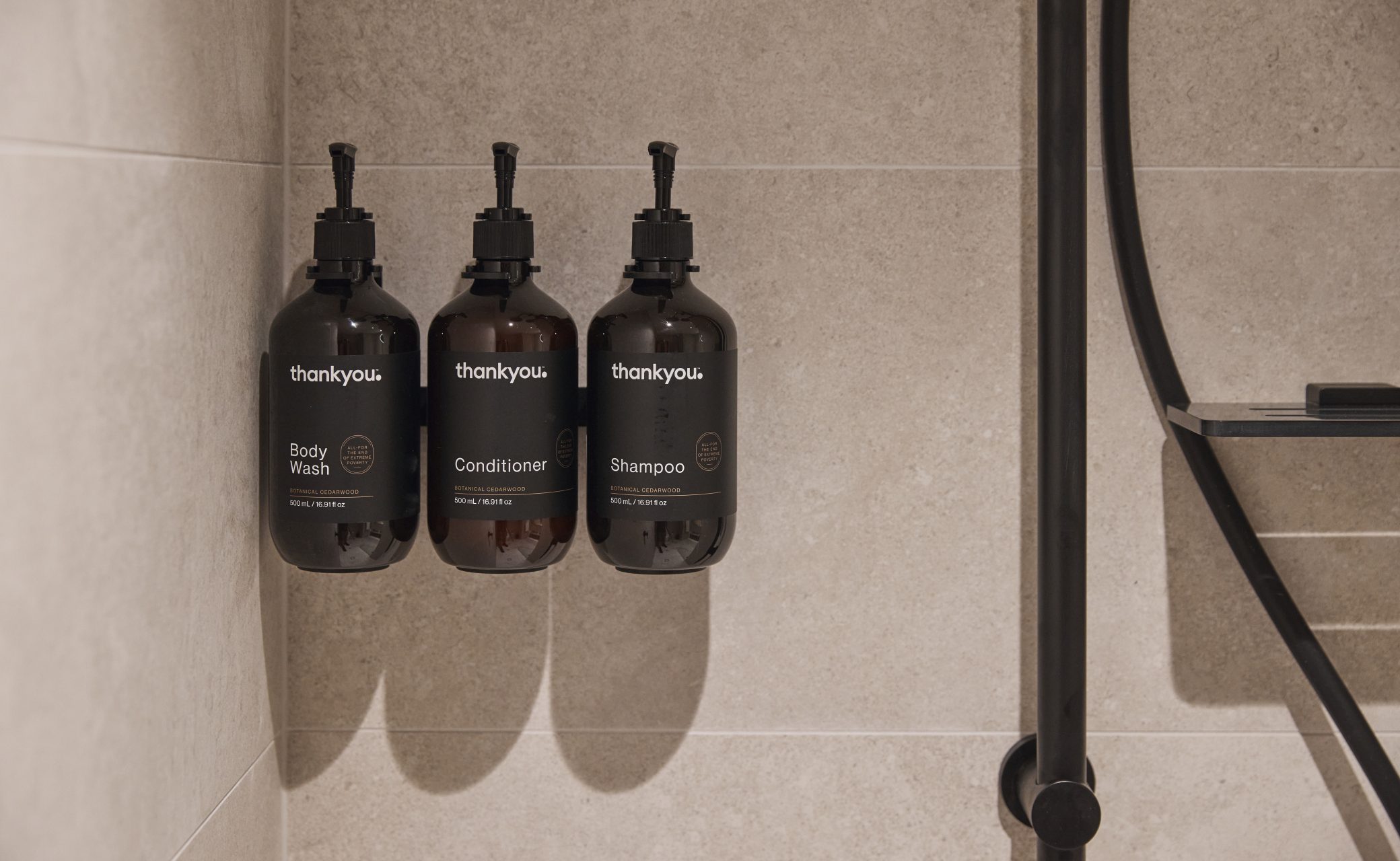 Three dark bottles labeled "Body Wash," "Conditioner," and "Shampoo" are mounted on a light-colored tiled wall.